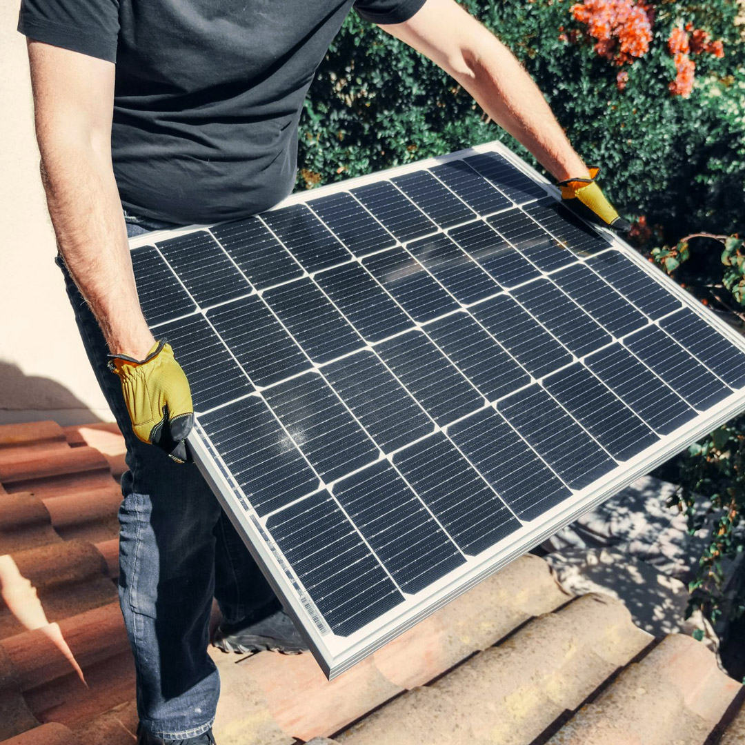 Una persona porta un panell solar mentre camina per un terrat